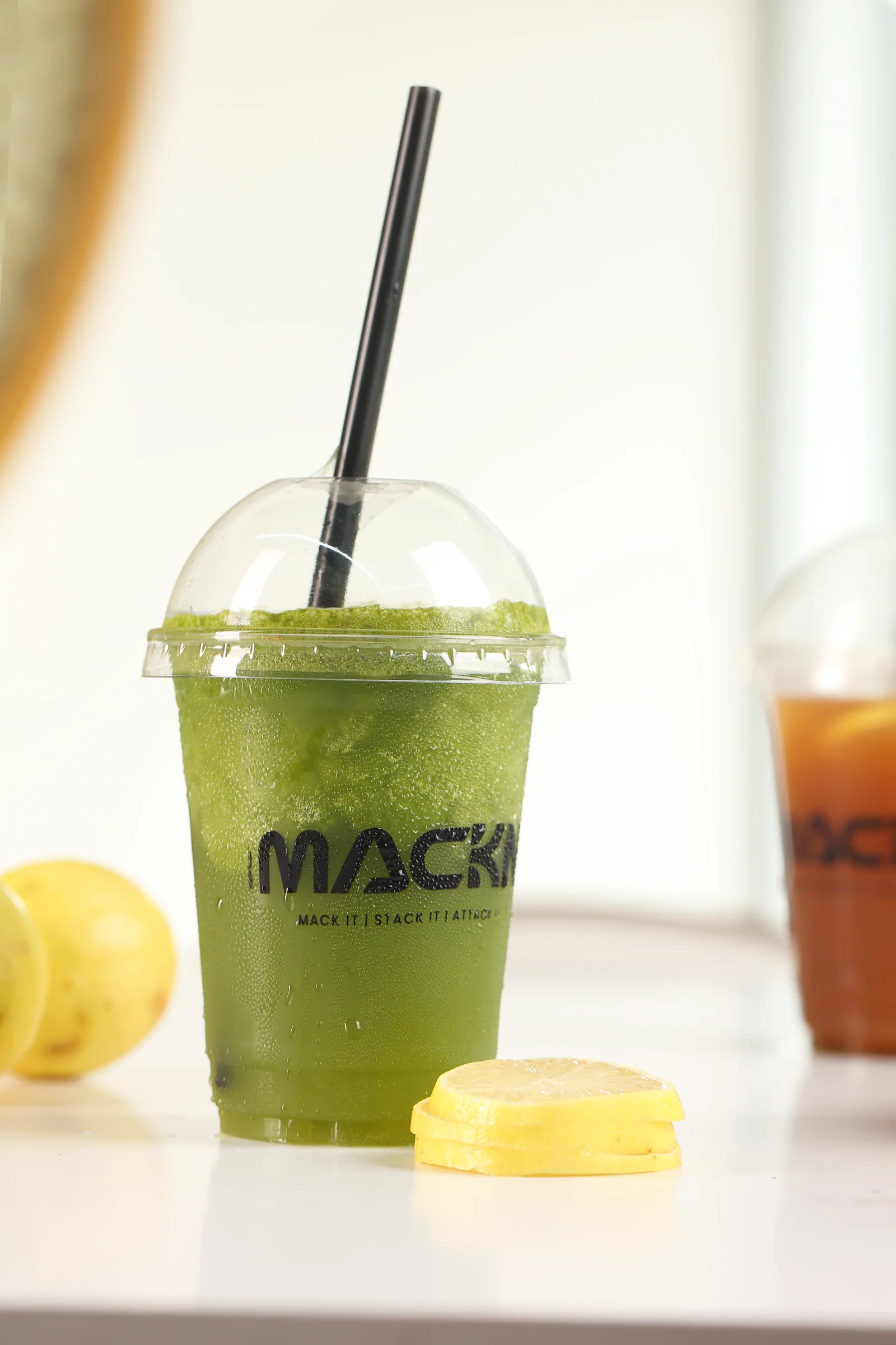 Bright green iced drink in a MACKN cup beside fresh lemons